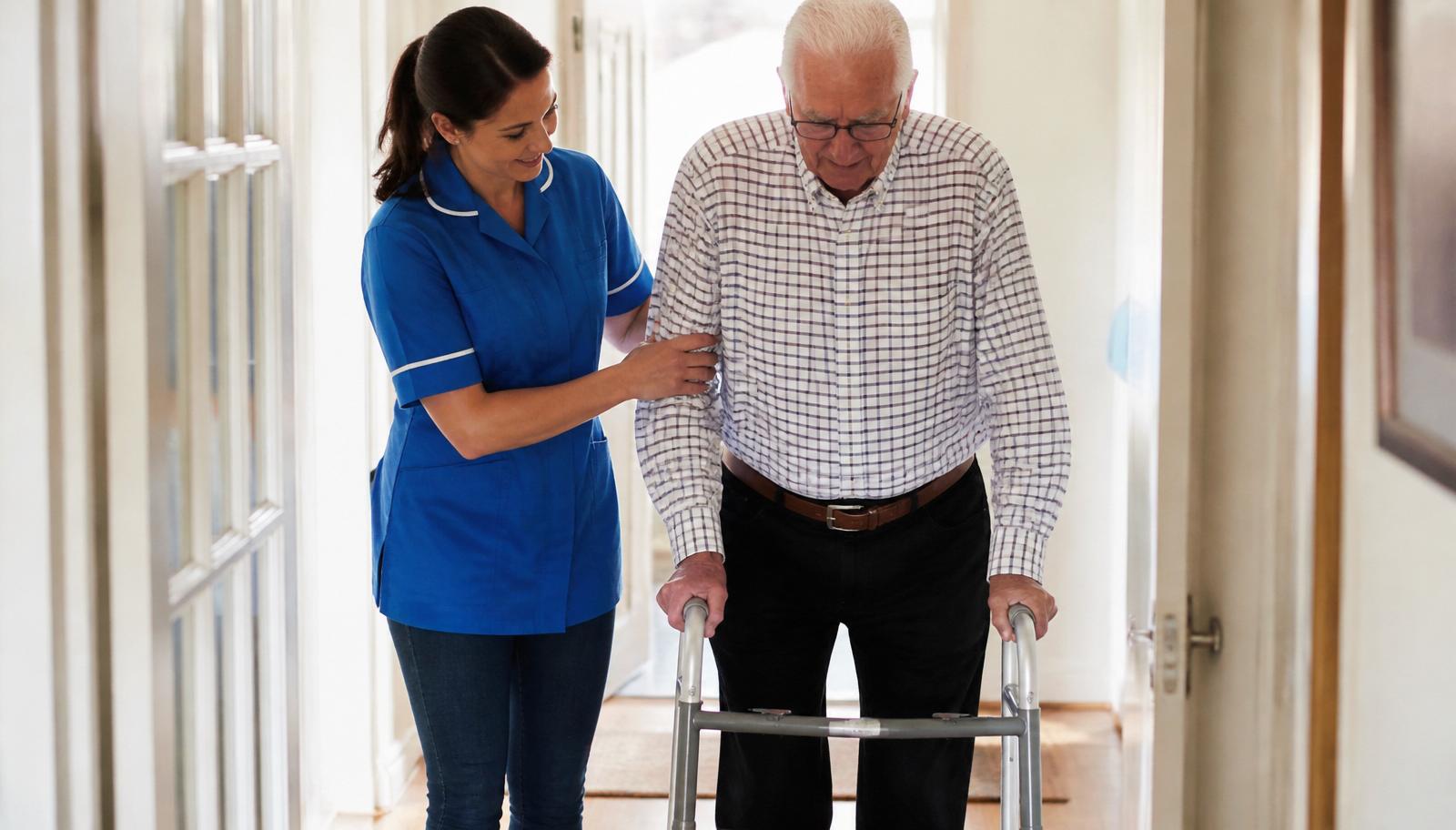 Nurse supporting an elderly man walking with a mobility frame at home